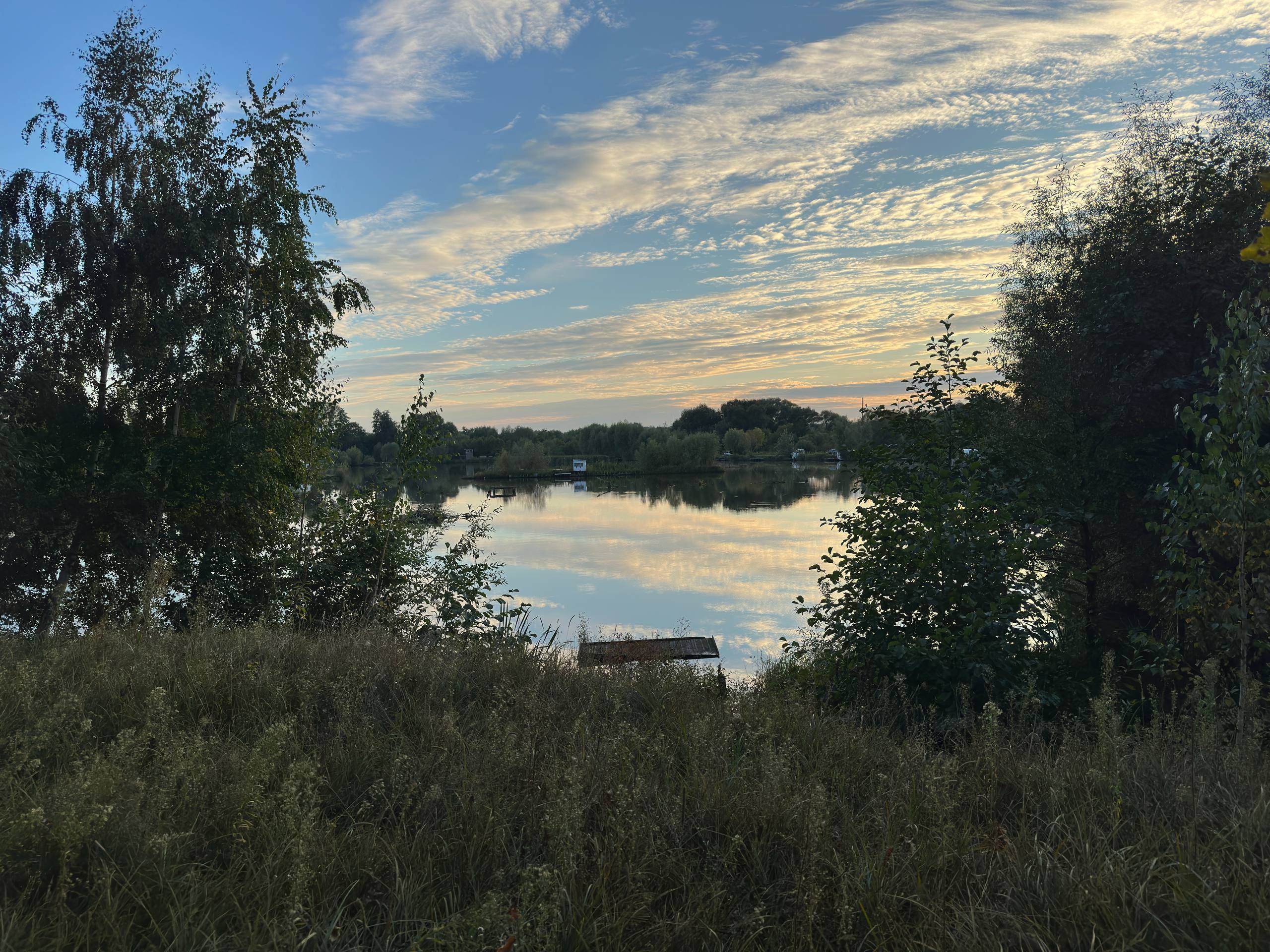 big pond with vegetation on the beach, small houses for fishing and beautifully mirrored sunset sky in the water